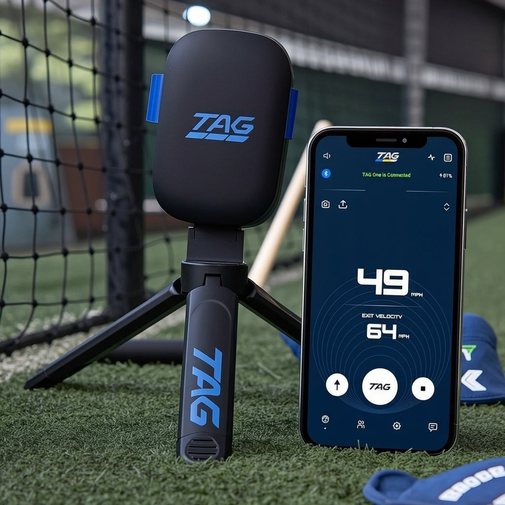 TAG sports radar device on a small tripod next to a smartphone displaying pitch velocity and exit velocity, set on turf in front of a hitting net.