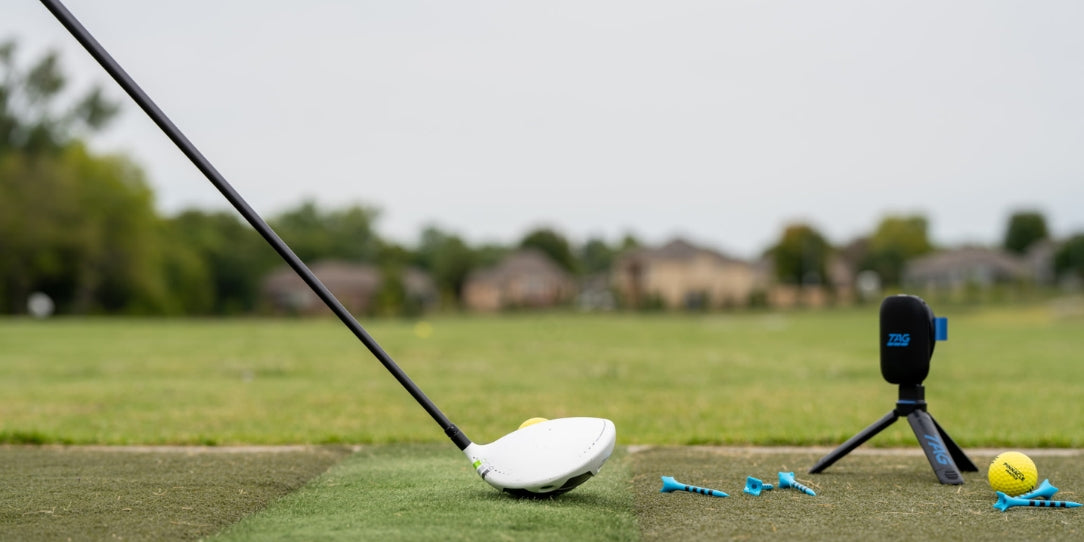 Golf club and ball on a tee with a camera on a tripod in the background