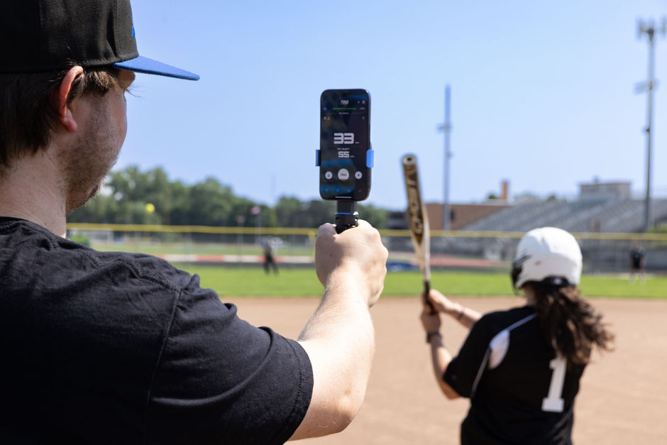 TAG One Sports Radar measuring pitch speed and exit velocity during softball training, featuring coach holding device and player swinging a bat.