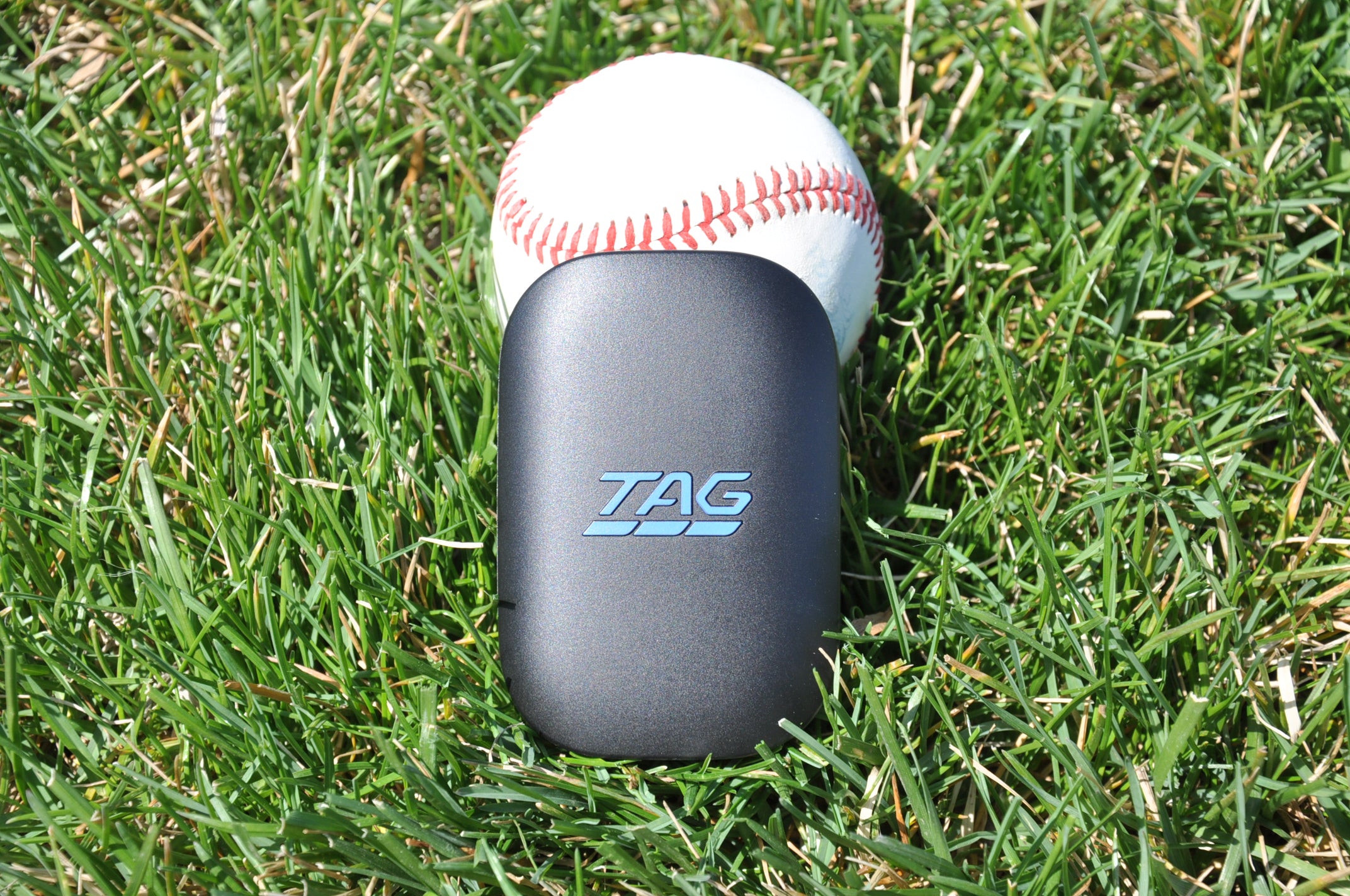 TAG One Sports Radar device leaning against a baseball on a grassy background.