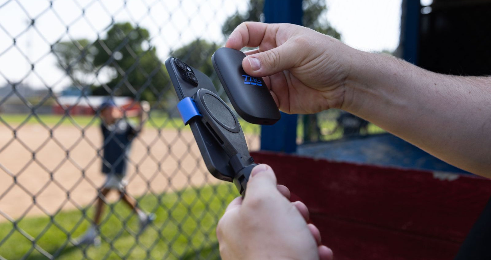 Person holding a device on a baseball field with a player in the background