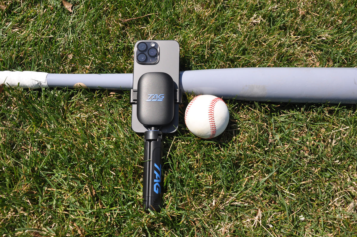 TAG One Sports Radar with phone and tripod, resting on grass next to a baseball bat and ball.