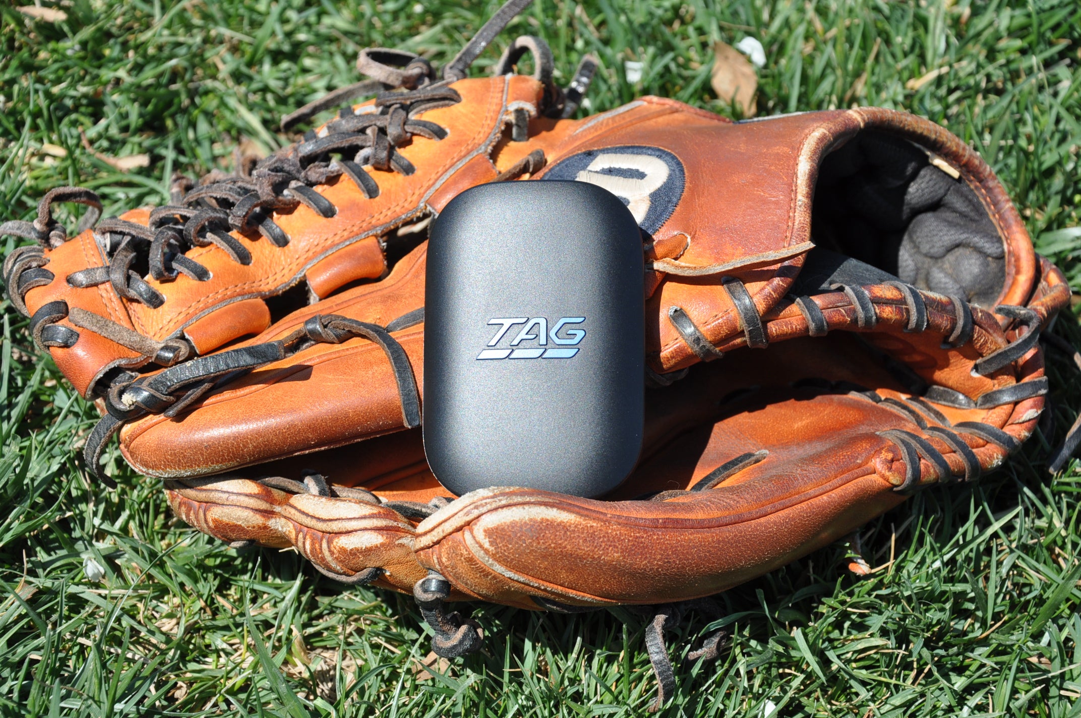 TAG One device laying on a Wilson baseball glove atop a grassy background.