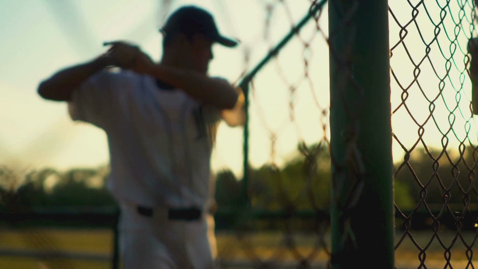 Baseball batter swinging a bat near a chainlink backstop.