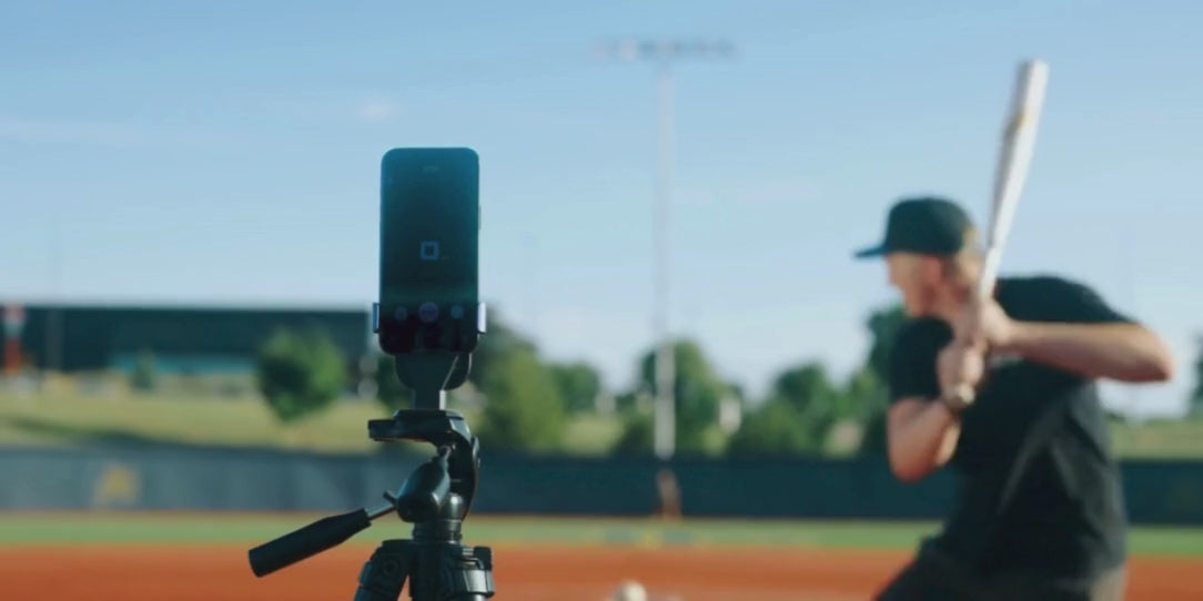 Baseball player hitting a ball off a tee while a radar tracks the hit's exit velocity.